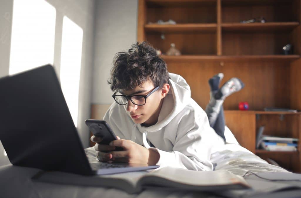 young boy studies lying on the bed using computer and smartphone homeschool planet image